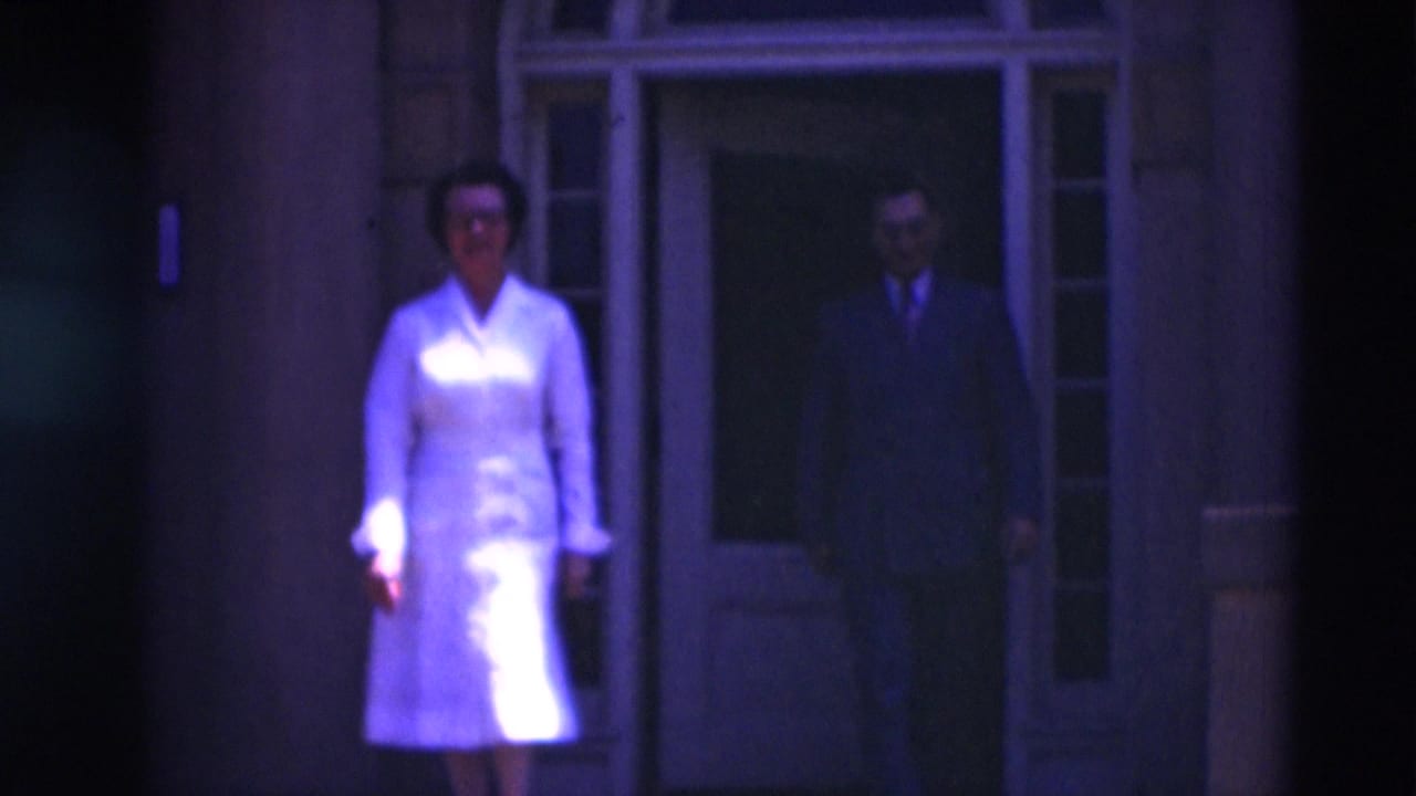 Woman in white exits ahead of a man in a dark suit at a building entrance.