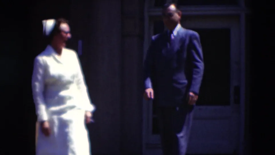 Near the end of the Paducah 1951 clip, the woman in white turns toward the suited man outside the shaded doorway.
