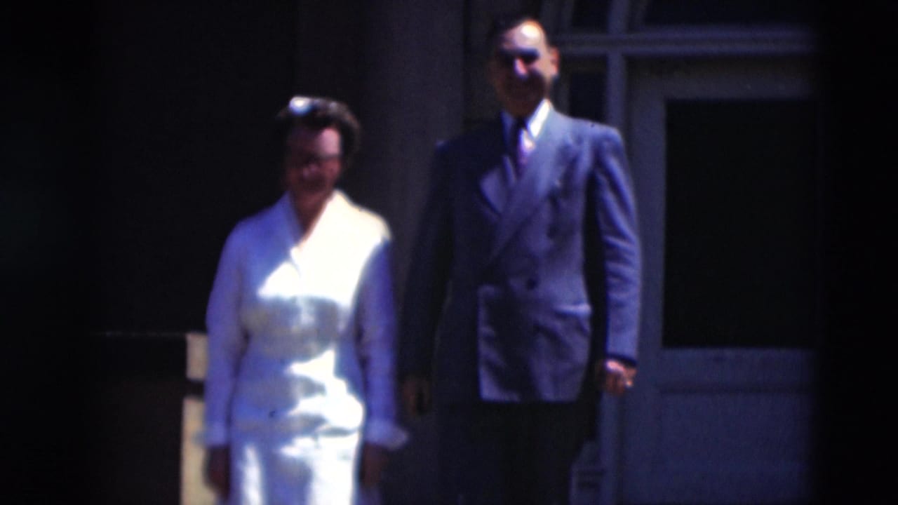 Woman in white uniform and man in dark suit walk side by side outside a building.