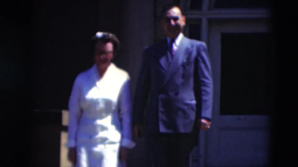The pair walks together outside a Paducah building, with the woman in white and the man in a dark suit partly lit by strong sun.