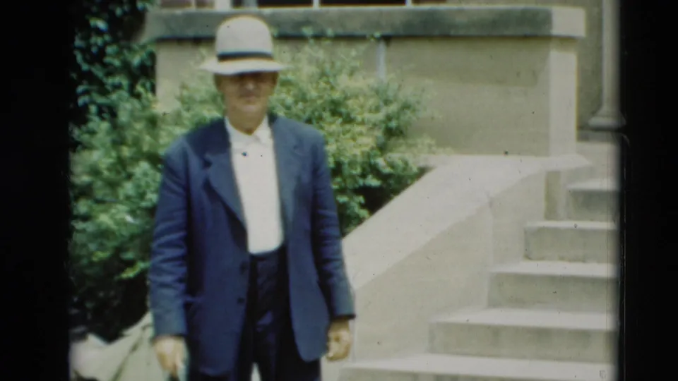 A man wearing a light fedora, white shirt, and dark jacket walks near stone steps in the 1951 Paducah footage.