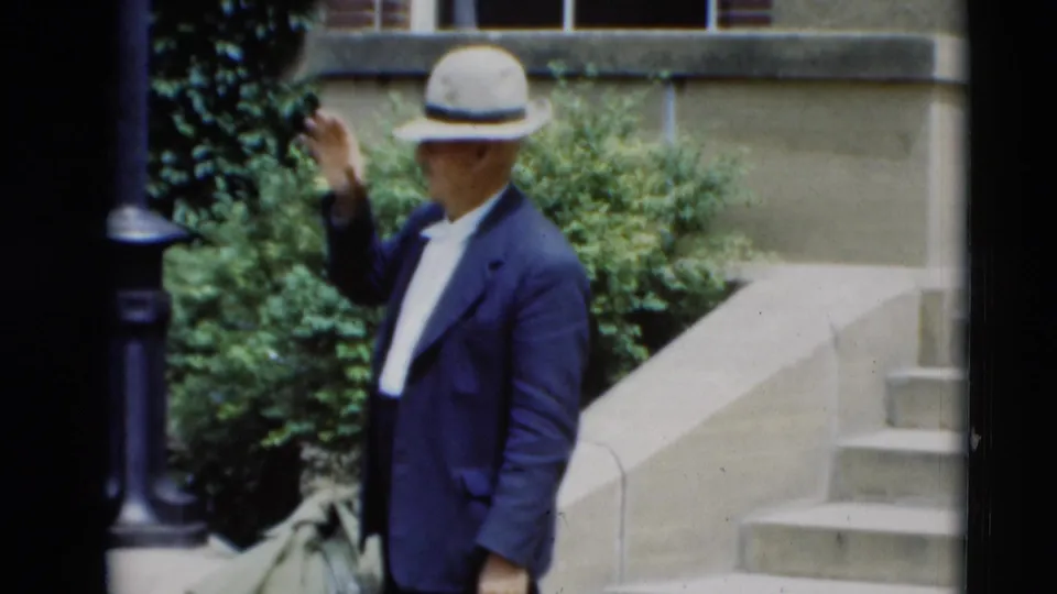 Adult man in a light fedora raises his hand toward the camera outside a Paducah building in 1951 footage.