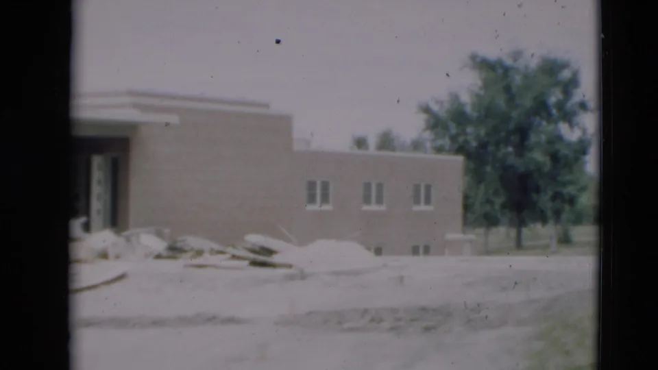 1951 Paducah, Kentucky 8mm frame showing a tan brick building under construction, with an open entrance, sand piles, and a tree behind it.