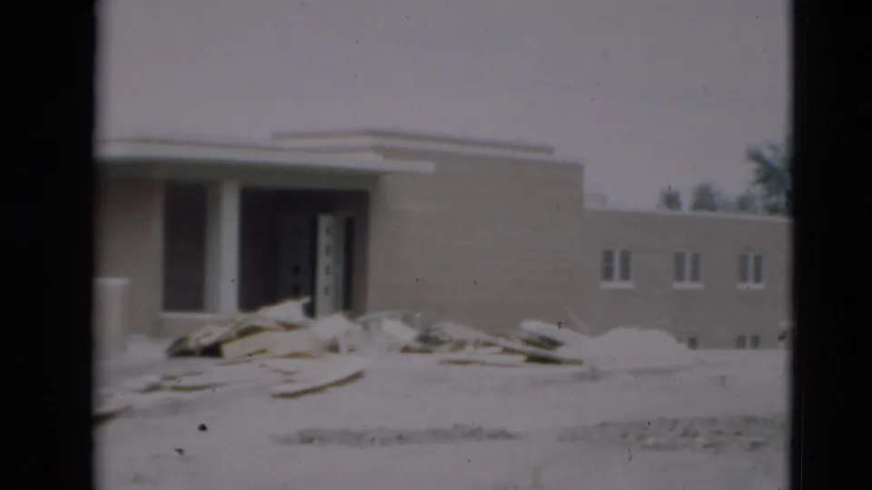 1951 Paducah construction view with a tan building facade, open doorway, white columns, scattered lumber, sand, and small windows.
