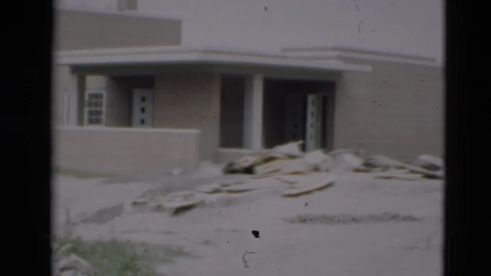 1951 Paducah 8mm frame showing a tan construction-site facade with a porch wall, columns, open doorway, windows, and lumber debris.