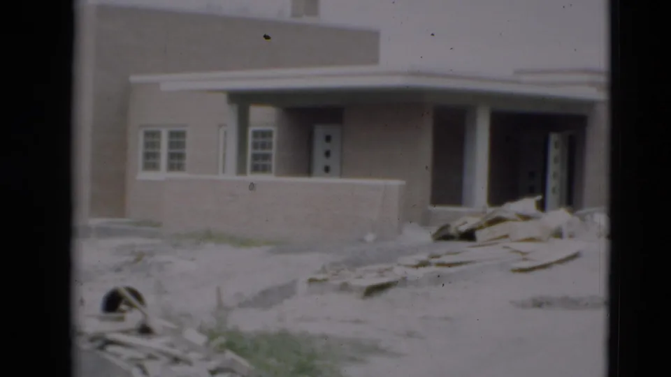 1951 Paducah frame of a tan brick building under construction, showing paired windows, an open entrance, porch columns, debris, and rough ground.