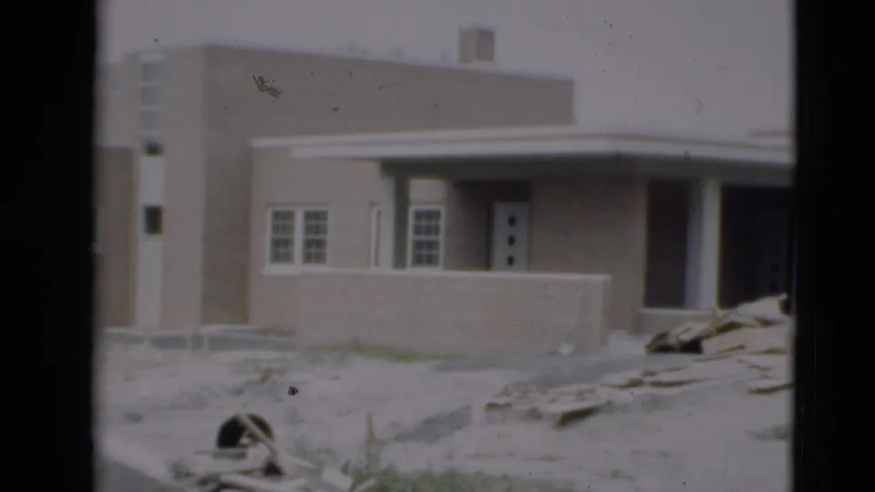 1951 Paducah home-movie frame showing a modern brick building with white trim, columns, dirt ground, and scattered construction materials.