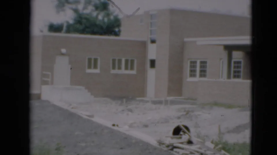1951 Paducah home-movie view from the side, with the building wall, driveway, railings, windows, and unfinished ground visible.