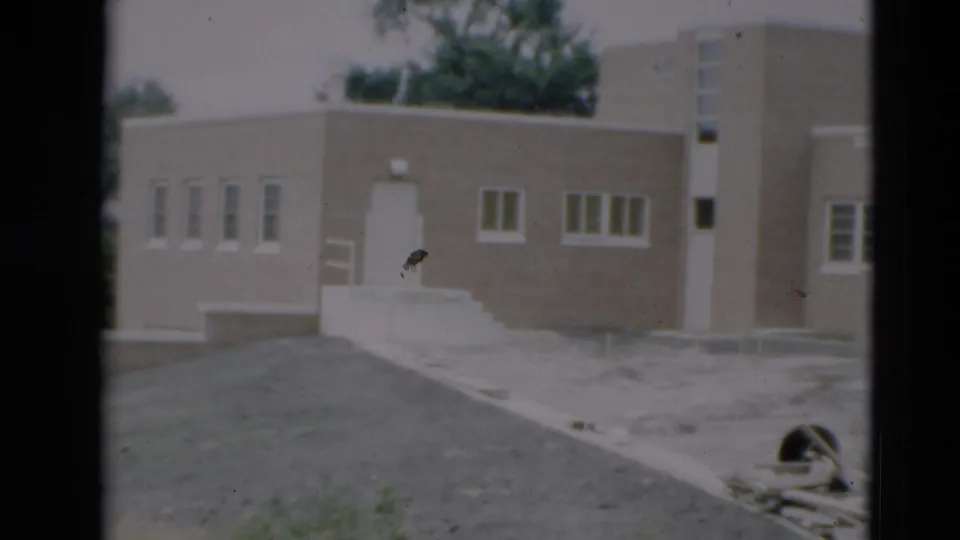 1951 Paducah frame showing the building from another side angle, with a paved drive, white railings, grouped windows, and debris nearby.