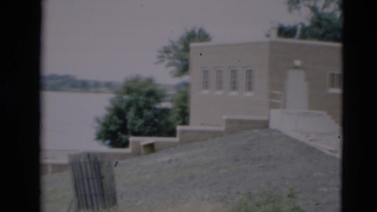 Flat-roof building beside trees with water visible beyond the grounds.