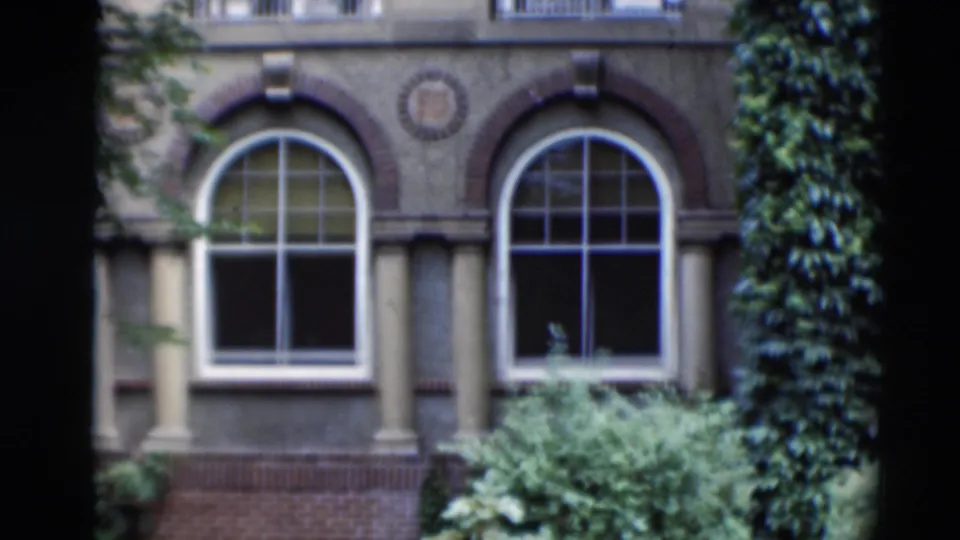 1951 Paducah footage showing two arched windows, brick trim, pale columns, shrubs, and foreground tree trunks framing the facade.
