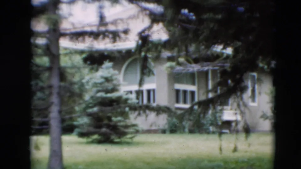 1951 Paducah frame showing the house facade, arched window, lawn, shrubs, and evergreen trees in soft 8mm focus.