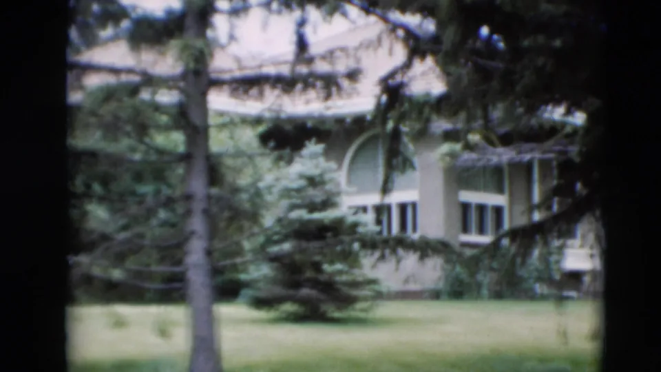 1951 Paducah home-movie frame showing a pale house with arched window details, lawn, and trees partly obscuring the facade.