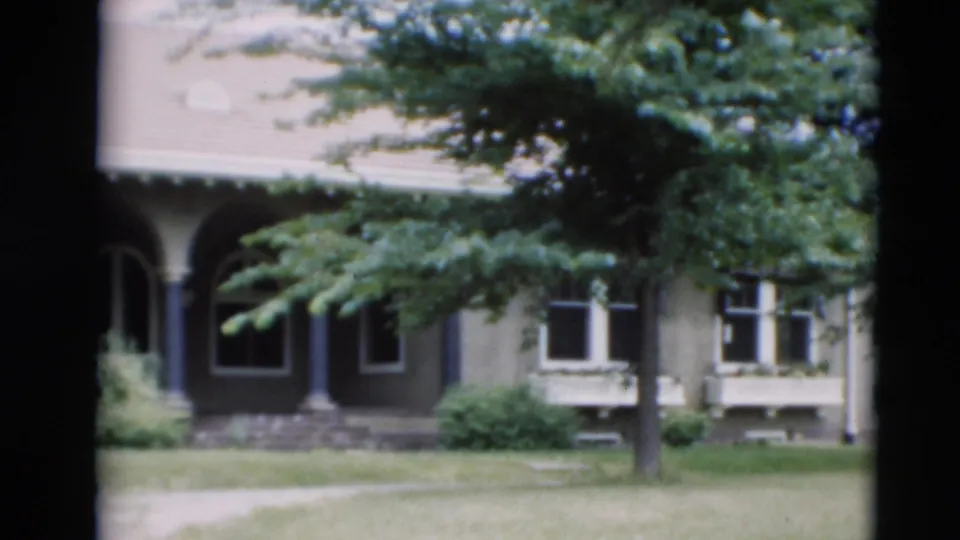 1951 Paducah home-movie frame showing an arched porch or entry area, house windows, lawn, trees, and low shrubs.