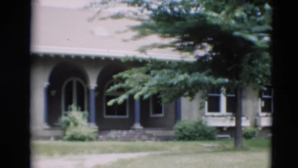 1951 Paducah home-movie frame showing a stucco house facade with an arched entry, dark shutters, trees, and front lawn.