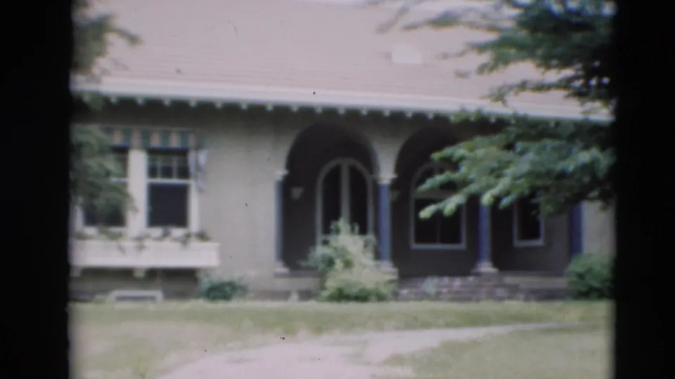 1951 Paducah frame showing the front of a suburban house with arched entryways, shuttered windows, trees, and grass.