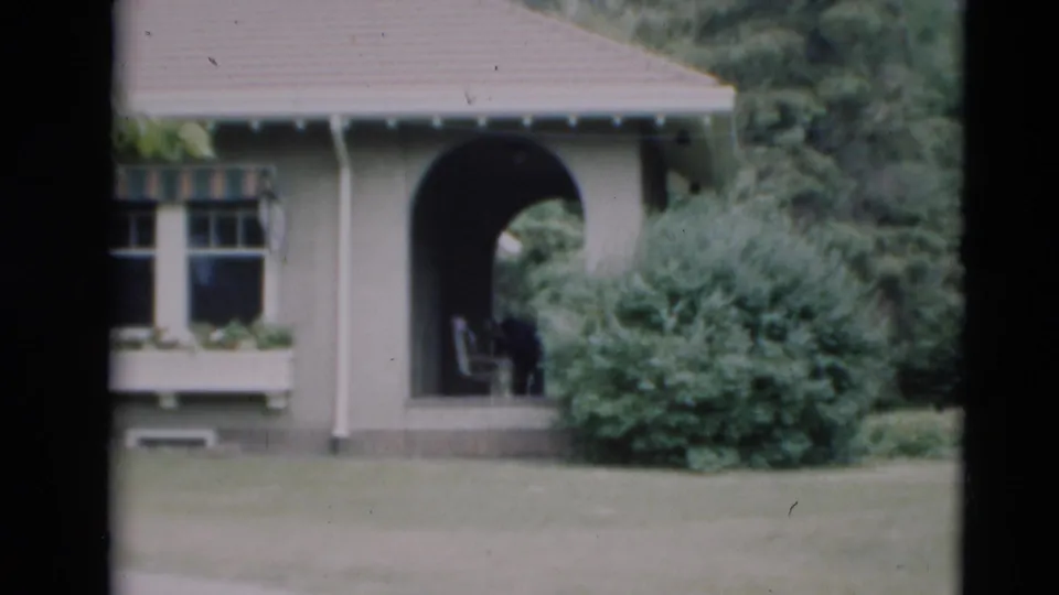 1951 Paducah home-movie frame showing a grey residential exterior with arched porch, divided window, lawn, and shrubs.
