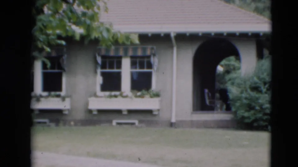 1951 Paducah frame showing the grey house more closely, with two divided windows, a white window box, arched porch, lawn, and shrubbery.