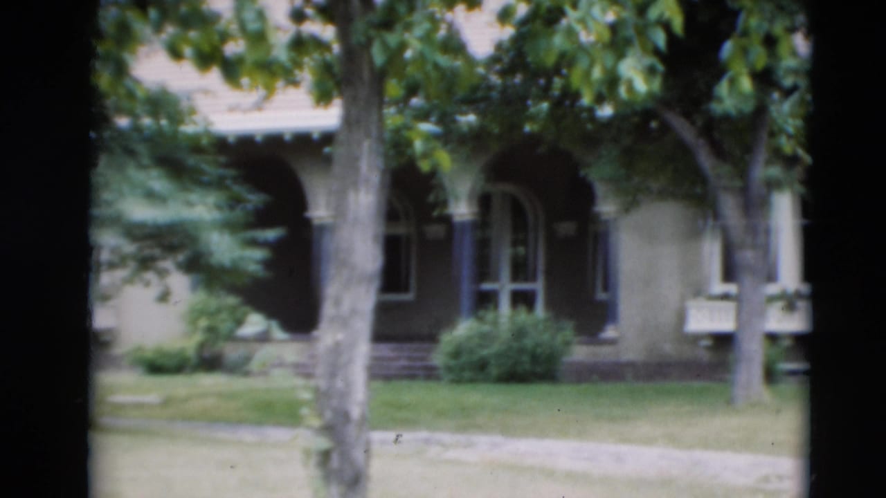 1951 Paducah home-movie frame of a finished house seen through trees, showing an arched entry, windows, lawn, and sidewalk.