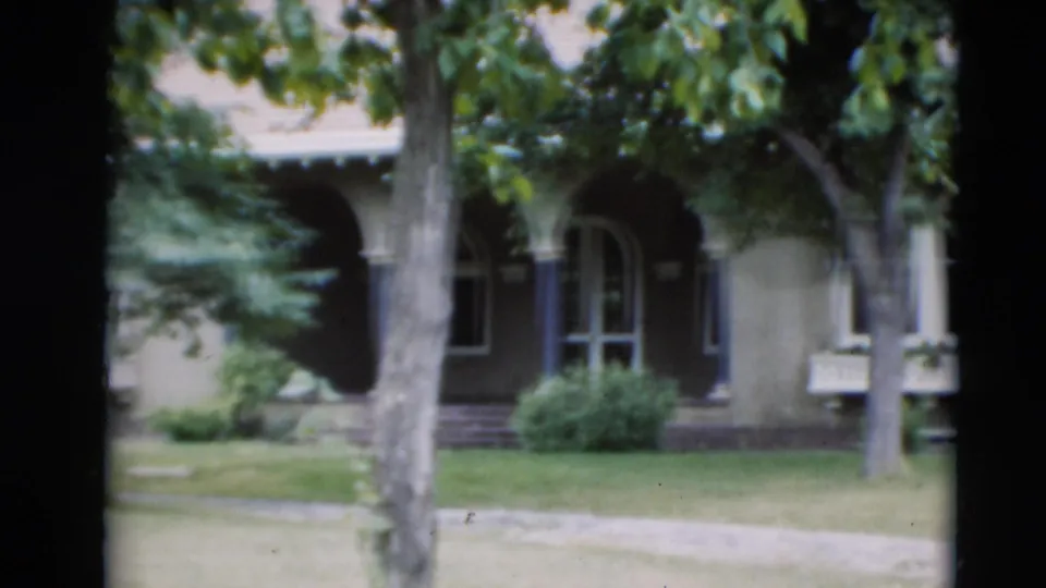 1951 Paducah home-movie frame of a finished house seen through trees, showing an arched entry, windows, lawn, and sidewalk.