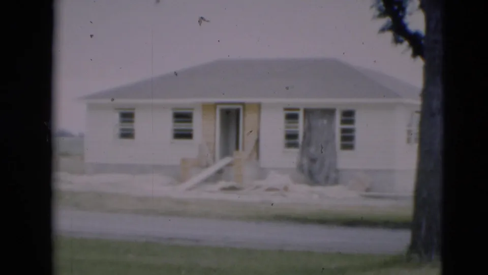 1951 Paducah home-movie frame of a modest house under construction, with exposed entry work, windows, a large tree, bare yard, and street.