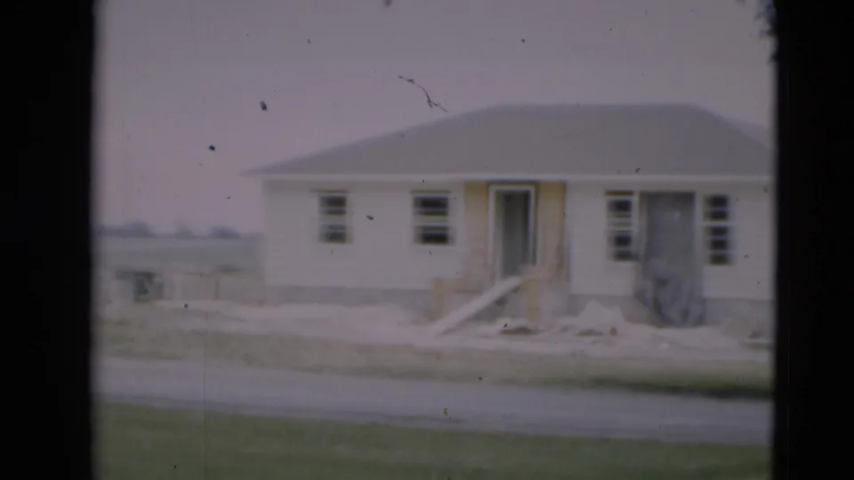 1951 Paducah home-movie frame showing a white one-story house with a gray roof, lawn, road, and soft 8mm grain.