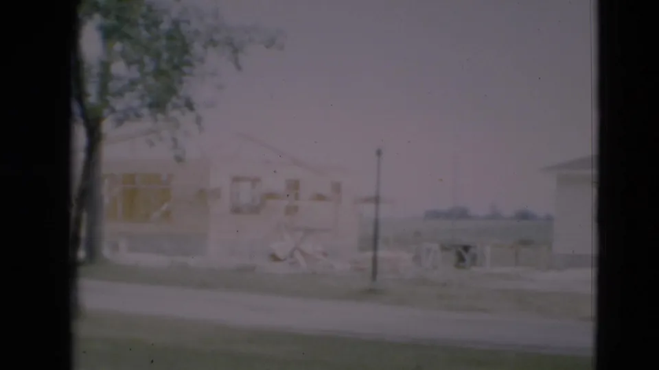 1951 Paducah home-movie frame with exposed house framing, a roadside utility pole, construction materials, grass, and a tree.