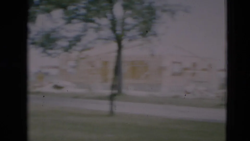 1951 Paducah frame showing a soft, panned view of a construction lot with tree branches, road, and partly built houses.