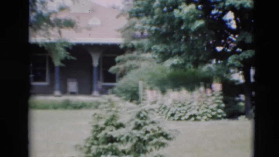 1951 Paducah home-movie frame showing a covered porch, support posts, windows, lawn, trees, and garden planting around the house.