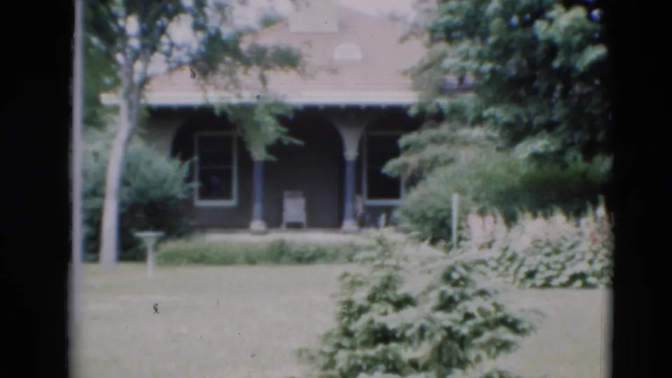 1951 Paducah residential exterior showing porch posts, windows, lawn, shrubs, mature trees, and a tiled-looking roof in soft color film.