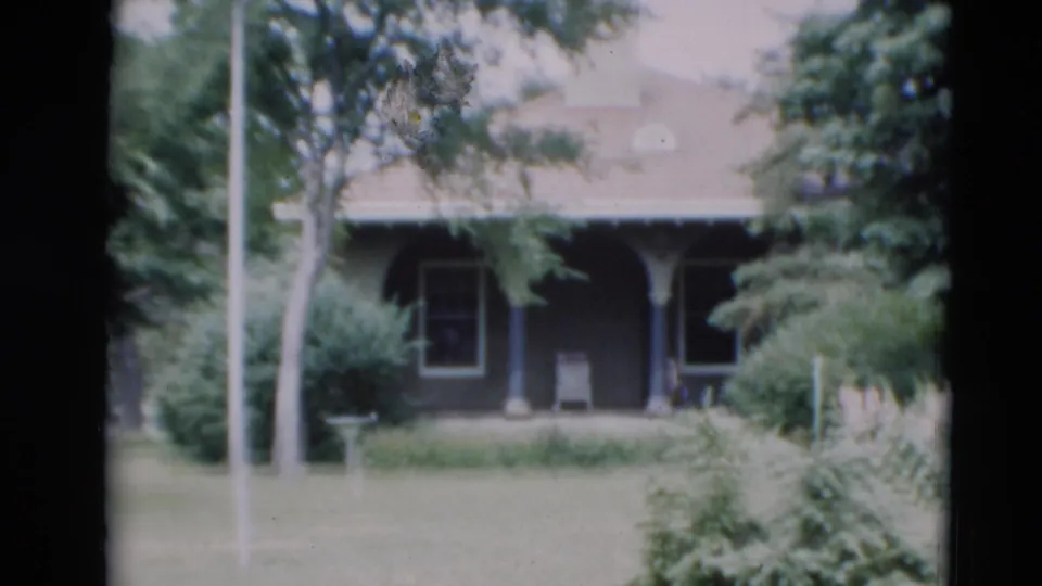 1951 Paducah home-movie frame showing a house porch partly screened by trees, with a lawn and birdhouse pole in front.