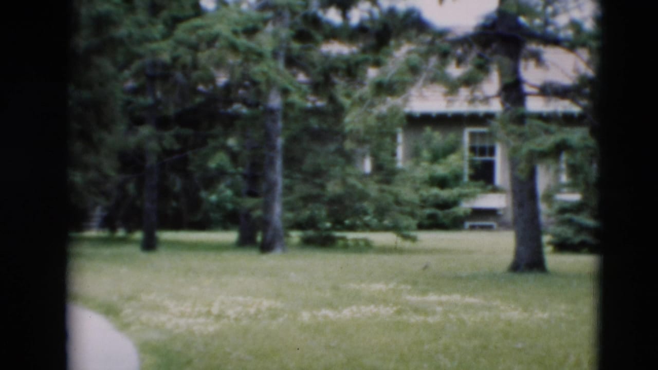 House and lawn seen through dark film-frame borders with trees in front.