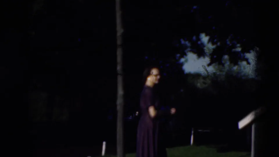 In this 1951 Paducah, Kentucky home-movie frame, a woman in a dark dress walks across a shaded lawn near trees.