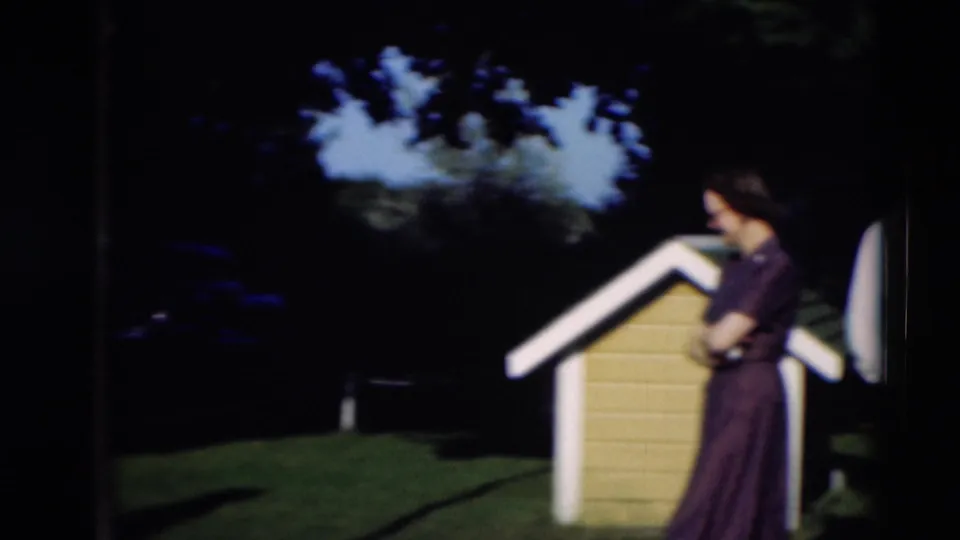 1951 Paducah home-movie frame with the woman beside the doghouse and the man partly visible at the right edge.