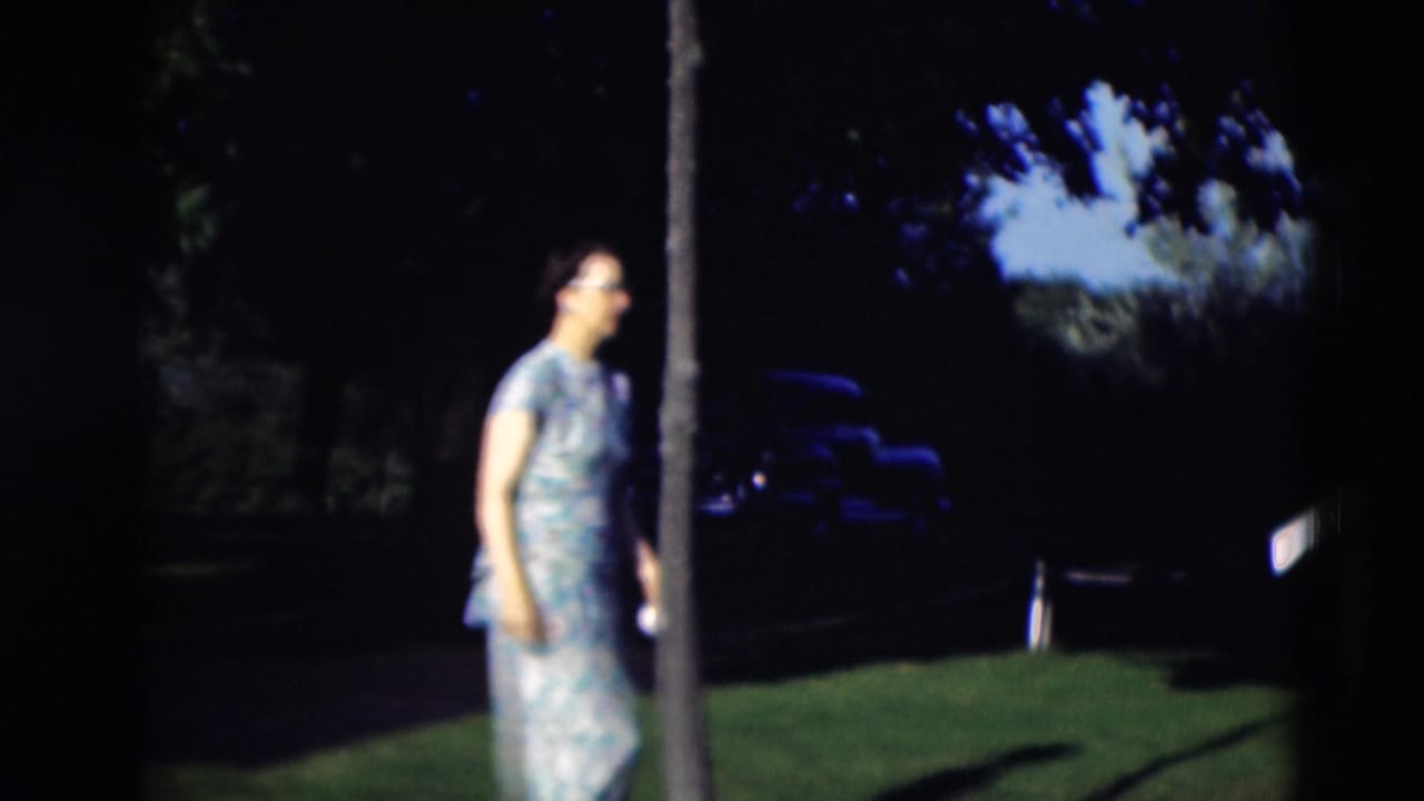 Woman in a patterned dress walking across a shaded lawn near trees.