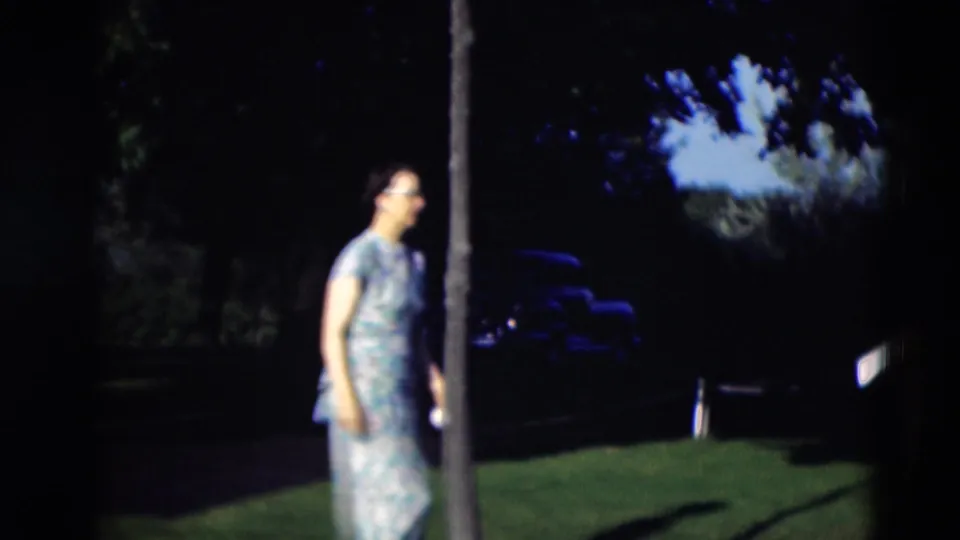 In 1951 Paducah home-movie footage, a woman in a light patterned dress walks across a shaded green lawn.