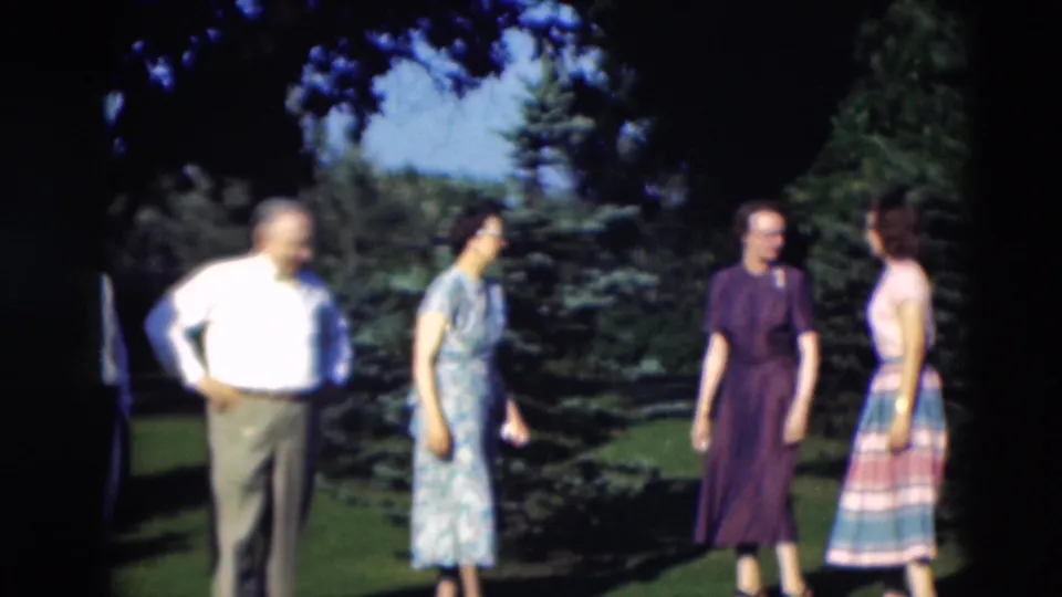 1951 Paducah home-movie frame showing adults in mid-century dress standing and talking on a shaded lawn.