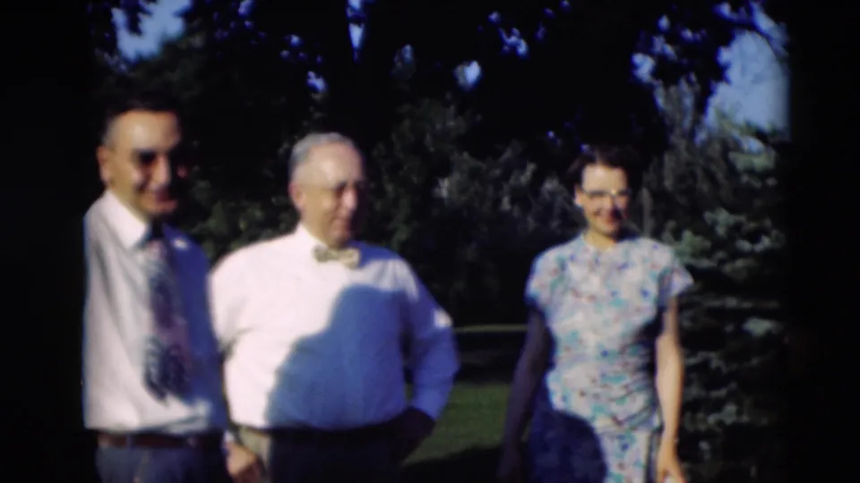 Soft 8mm frame from Paducah in 1951 showing three adults standing in a sunny yard with trees behind them.