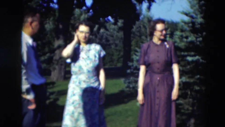 1951 Paducah home-movie frame showing a man and two women outdoors, casually posed among evergreen trees and lawn.