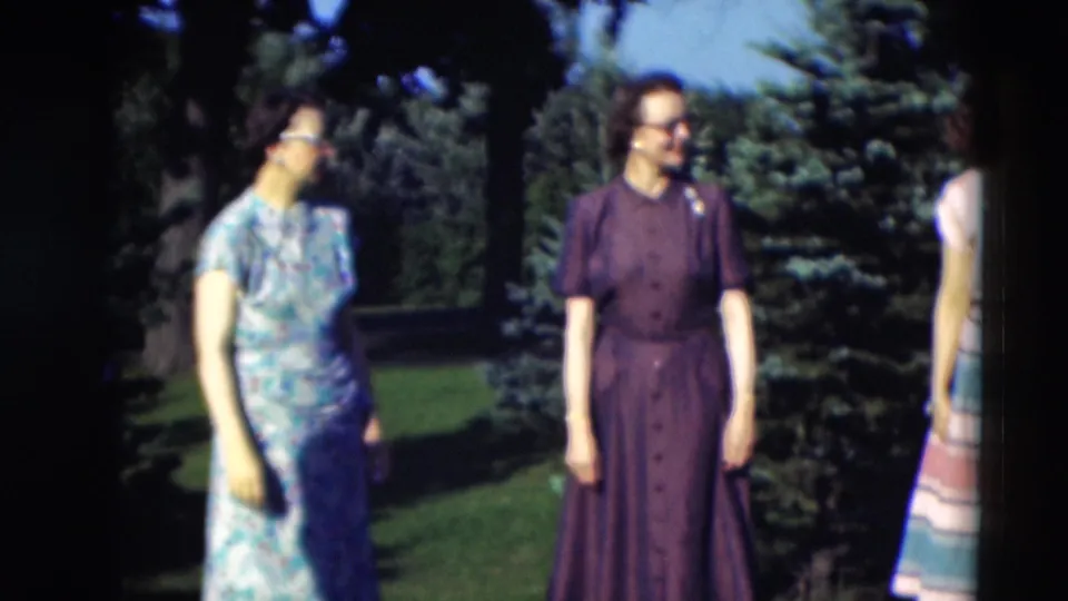 1951 Paducah frame showing two women in dresses turned toward each other in a garden, with another figure partly visible at right.