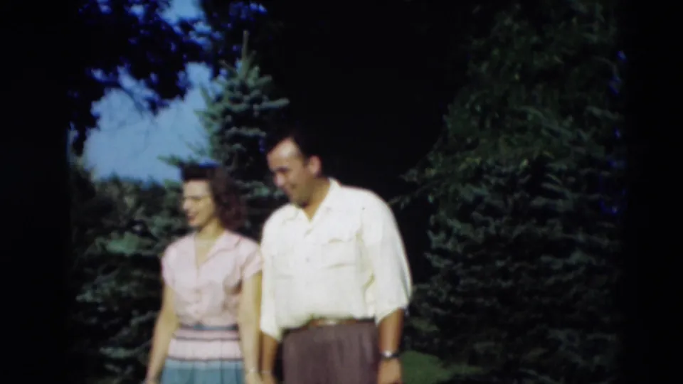 1951 Paducah home-movie frame showing a couple walking closely outdoors with evergreens and lawn behind them.