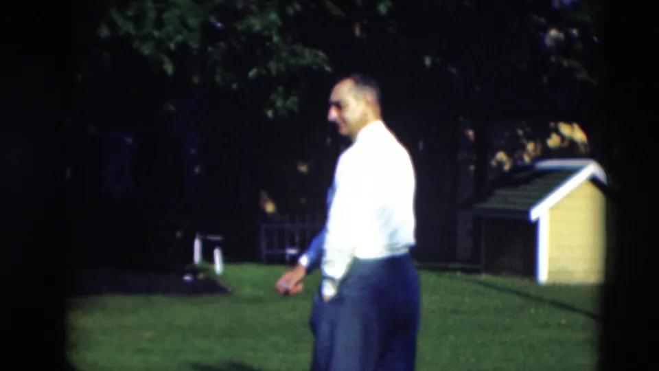 The man turns partly toward the camera, showing a tie, glasses, white shirt, and dark trousers on the Paducah lawn.