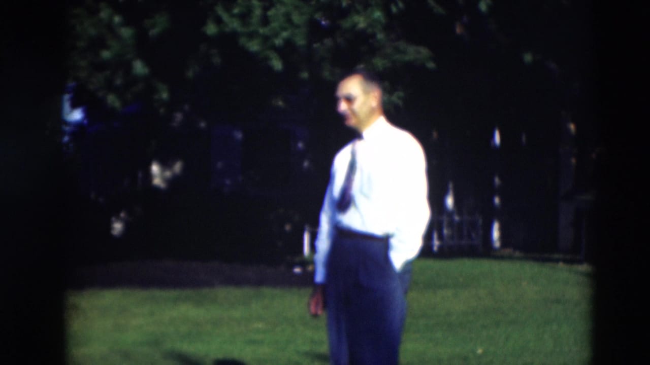 In 1951 Paducah home-movie footage, a man in a white shirt and tie stands on a sunny lawn with trees behind him.