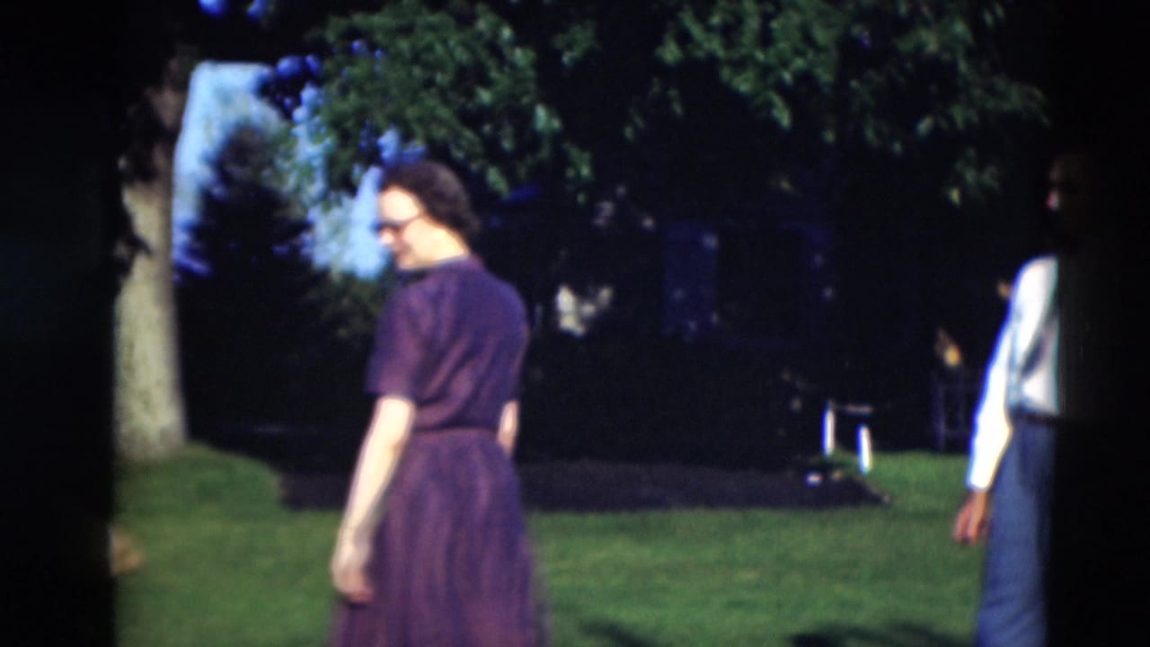 A woman in a dark purple dress walks across a green lawn in the 1951 Paducah home-movie scene.