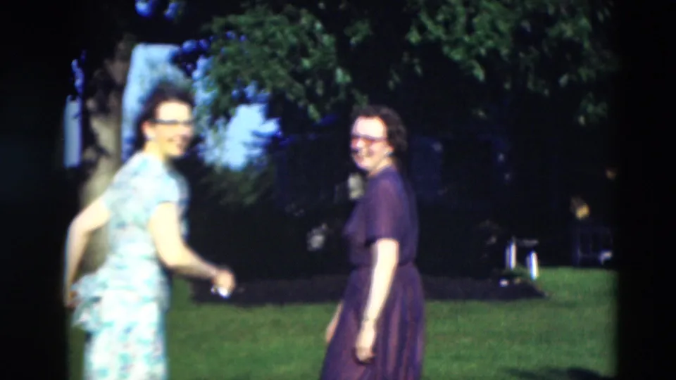 Two women, one in a floral dress and one in a dark dress, turn toward the camera on a Paducah lawn in 1951 footage.