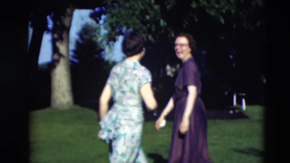 Two women in 1950s dresses approach a man partly visible at the edge of the frame on a green Paducah lawn.