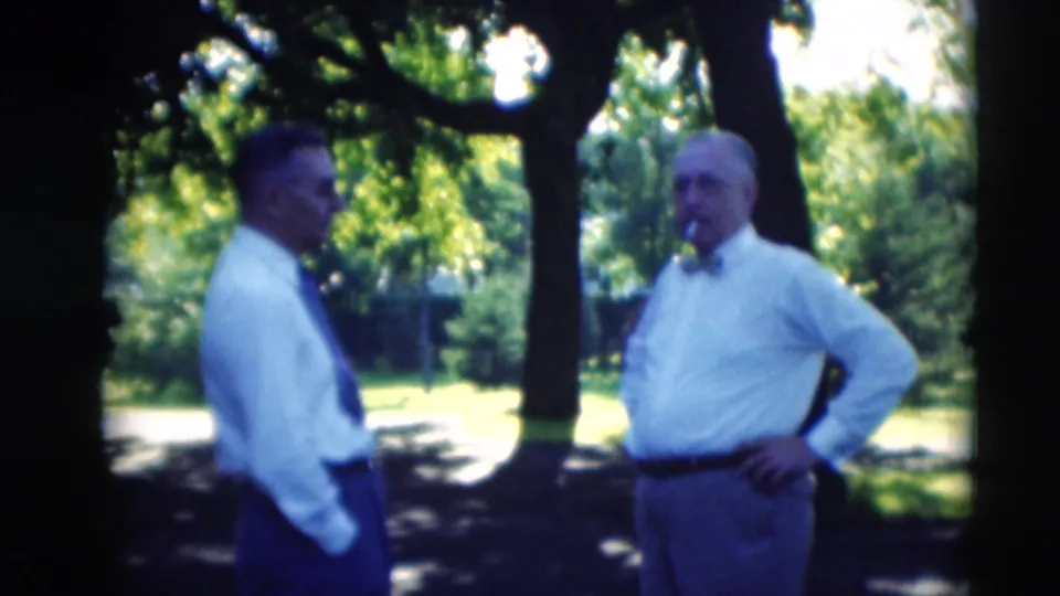 Two well-dressed men converse in shade under leafy trees in 1951 Paducah, Kentucky home-movie footage.