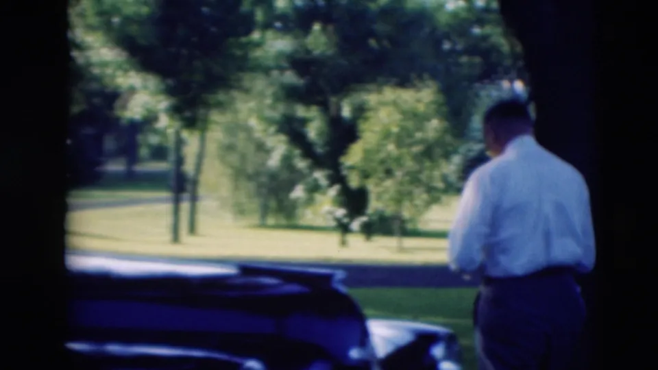 The man walks away from the black car toward a sunlit grassy area, consistent with the Paducah 1951 home-movie setting.