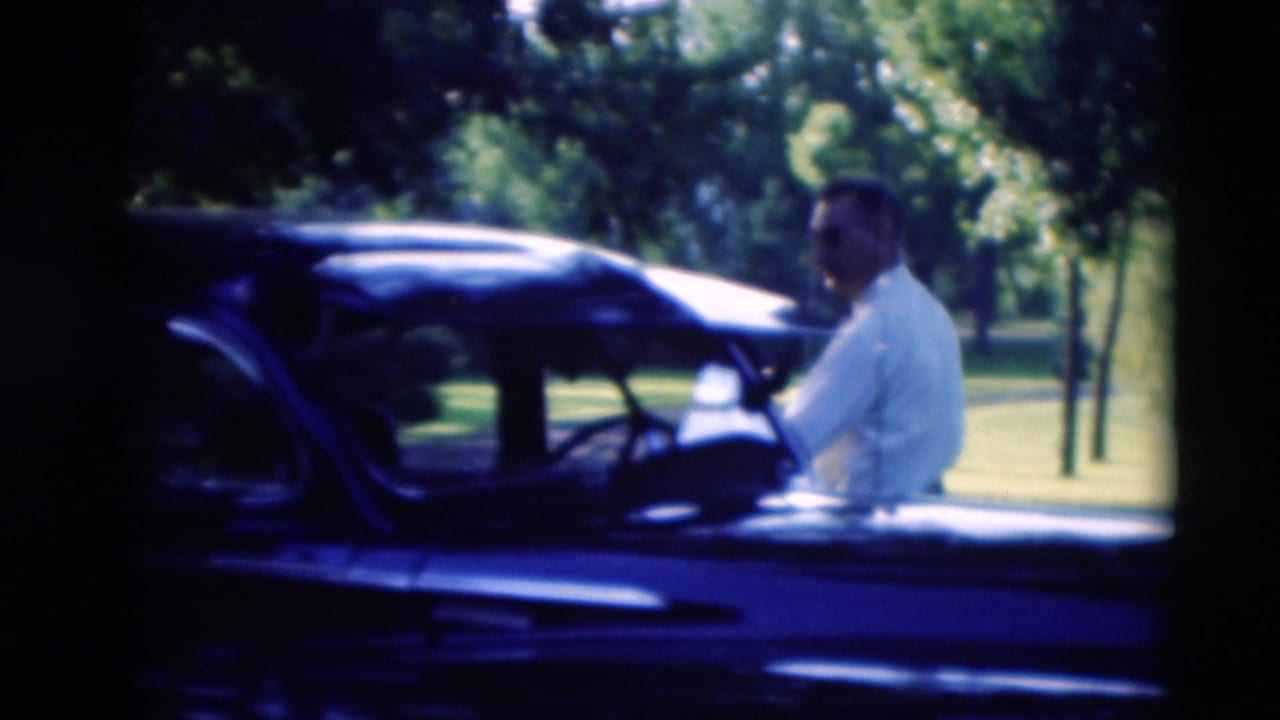 A man in a light shirt prepares to enter a dark car in a 1951 Paducah park scene, with grass and trees in the background.