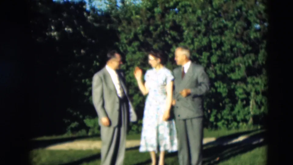 In the supplied 1951 Kentucky home-movie frame, three adults stand together on grass, with trees and long shadows behind them.